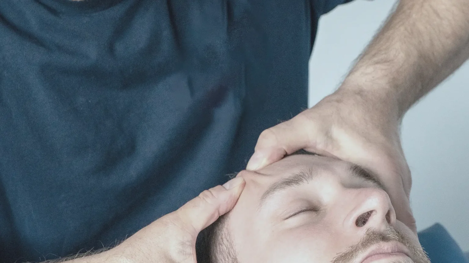 Dirk Weissensel behandelt einen Patienten in Rückenlage mit beiden Händen am Kopf